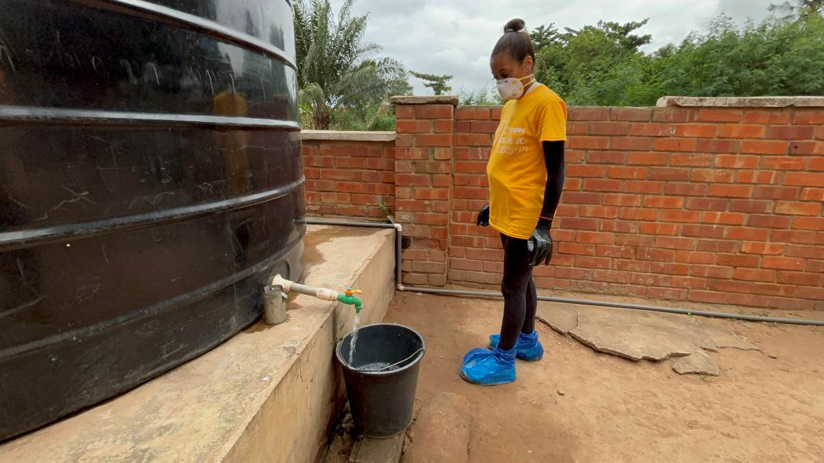 TAG IN Event: Mission Trip to Accra, Ghana! Volunteer in a yellow TAGIN Ghana Mission shirt collecting water from a tank into a bucket during community service.