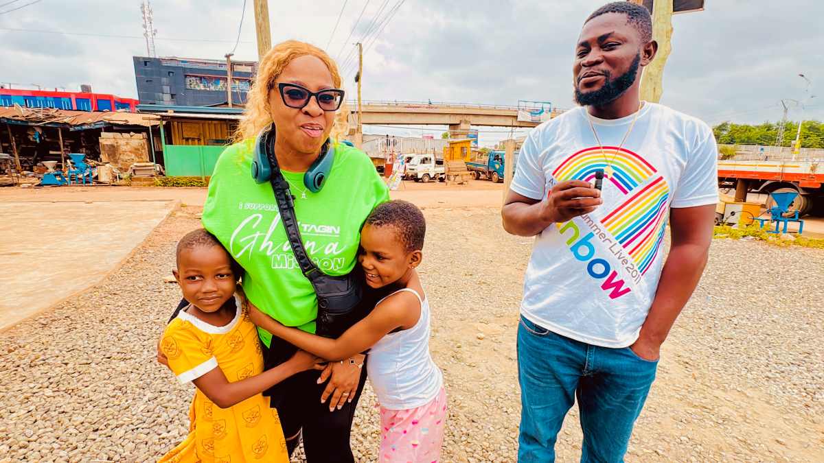 TAG IN Event: Mission Trip to Accra, Ghana! TAGIN Ghana Mission volunteer smiling and hugging two children in a Ghana community setting.